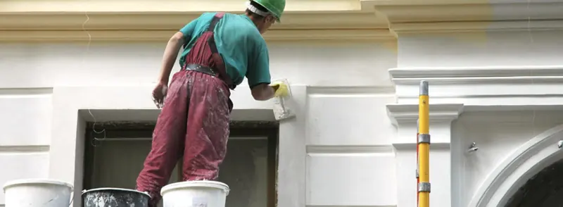 Painter brushing fresh white paint onto the ornate trim of a commercial building facade in Sarasota, FL