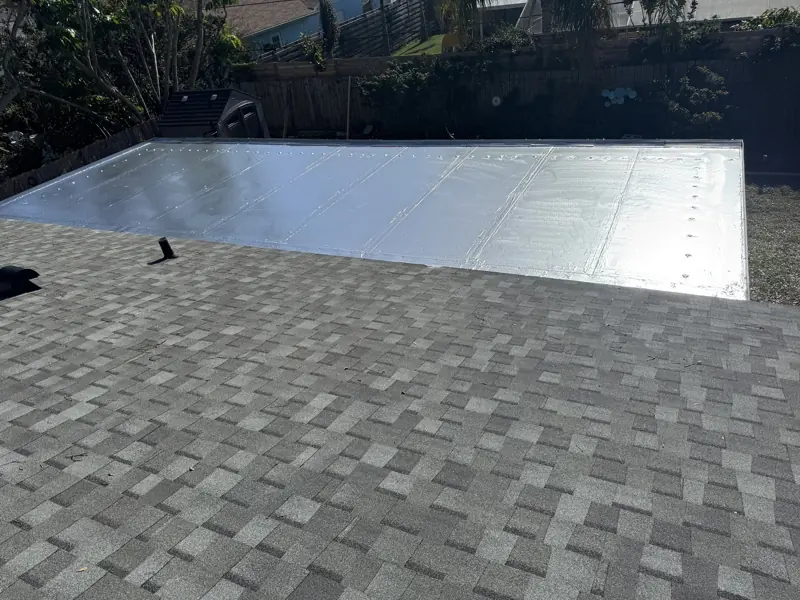 Flat roof section after painting with a silver finish beside a shingle roof