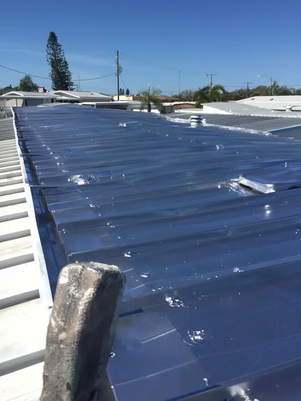 Metal roof painting in progress on a mobile home, first panels painted silver