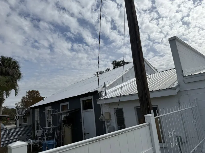 Metal roof painting in progress on a home with a white fence
