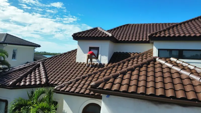 Painter spraying a brown tile roof on a two-story home