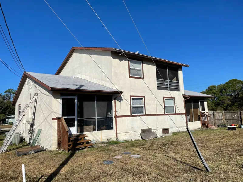 Rear of a two-story duplex before exterior painting, faded tan stucco with brown trim