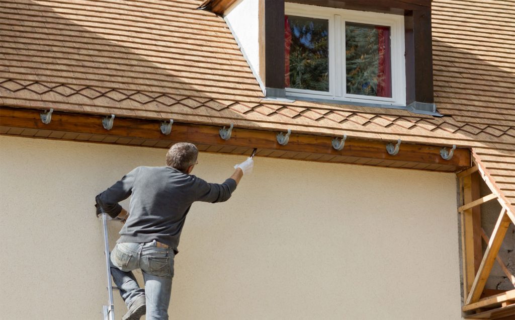 A man on a ladder painting the exterior of a house