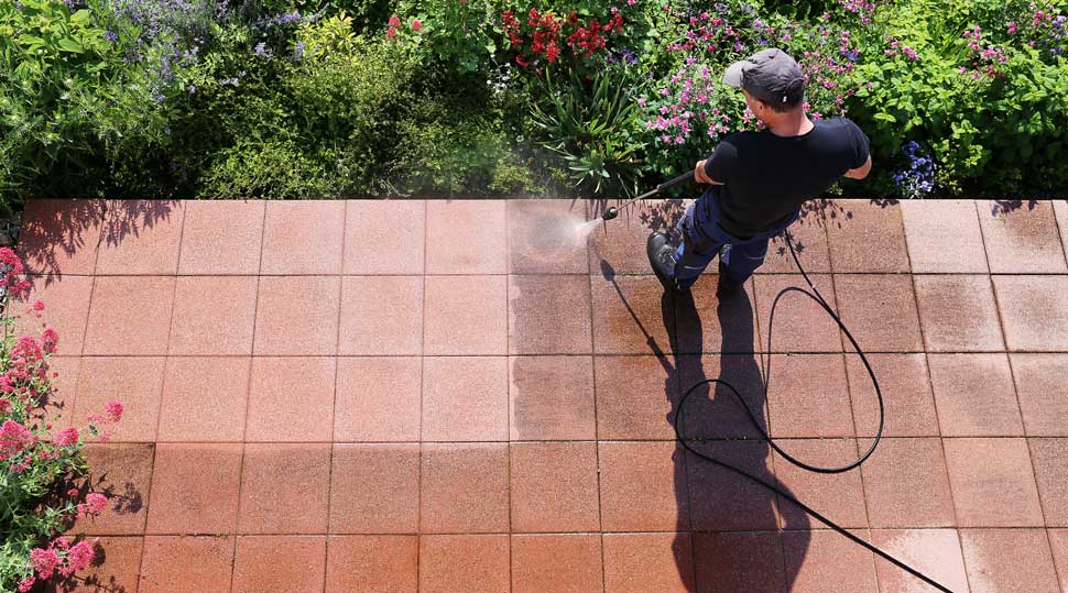 A man pressure washing a paved patio